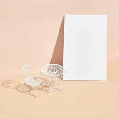 White metal table and chair on beige background. Minimal creative layout with sunshine and hard shadow. Palm leaves shadow and white paper blank. Cafe, restaurant, social distancing minimal concept