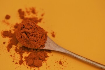 Red pepper powder in a wooden spoon on a  yellow background. Seasoning and spices. Hot spices