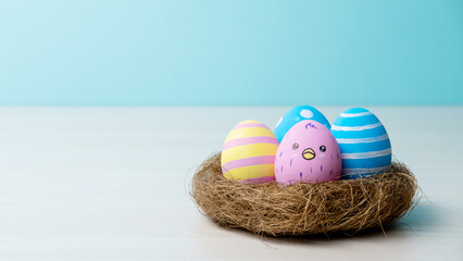 Easter holiday. Festive composition. Homemade ornament. Gift card. Pastel color arrangement of painted pink blue yellow eggs with cute chicken pattern in nest isolated on light copy space background.