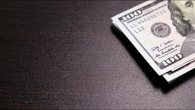Shrinking stack of hundred-dollar bills on wooden surface of desk. Space for text. Concept of losses, unsuccessful investments. Stop motion shooting