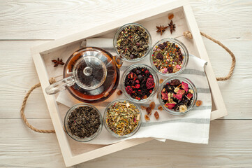 several varieties of herbal and berry tea and a kettle with hot fresh tea on a wooden tray and a white wooden table View from above.