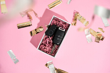 Going to make her really happy. Top view of a car key in gift box and shiny golden confetti on pastel pink background