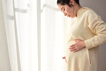 A pregnant woman in her twenties is holding her hand on her enlarged belly.