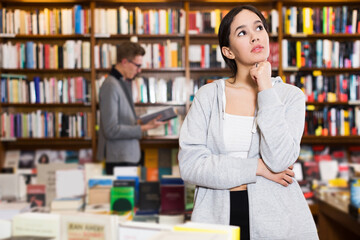 Portrait of young pensive attractive girl in interior of bookstore