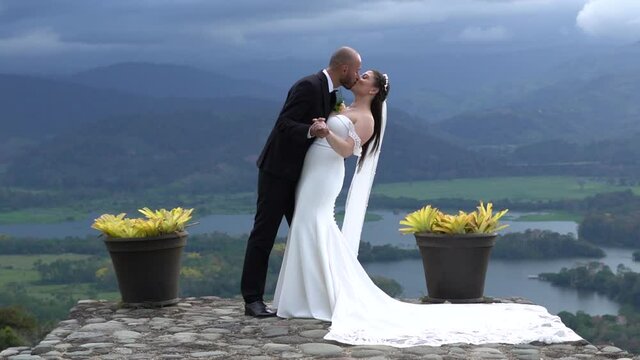 The groom giving a long, romantic kiss to the bride on their wedding day. Background: cloudy mountains, dreamy scenery.
