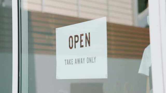 Young woman owner puts a OPEN take away only sign on the front door. Cafe or restaurant Affected by coronavirus disease.