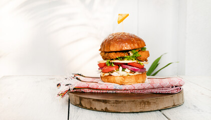 Burger z kurczakiem na jasnym tle, drewnianym stole w świetle dziennym. © insomniafoto