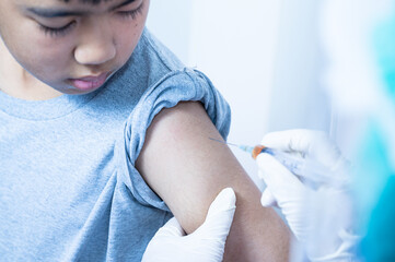 Fototapeta premium Doctor's hand injecting for vaccination in the shoulder kid patient.Vaccine for protection Coronavirus (Covid-19) infection with Asian boy.Vaccination for coronavirus treatment.