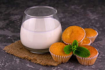 A glass of milk and small muffins on a gray background.
Close-up.