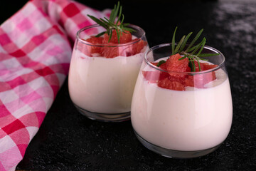 Two yoghurt with grapefruit in glasses on a black background.