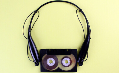 Black audio cassette with black wireless headphones on yellow background