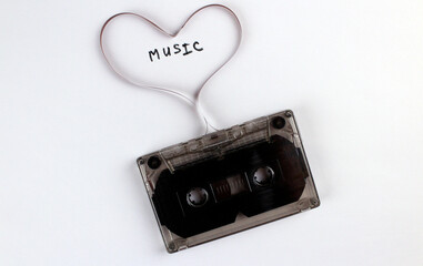 Old black audio cassette on a white background with a movie heart. Cassette heart with the word "music"