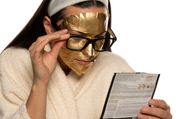 young woman with golden mask reading instructions from the product packaging