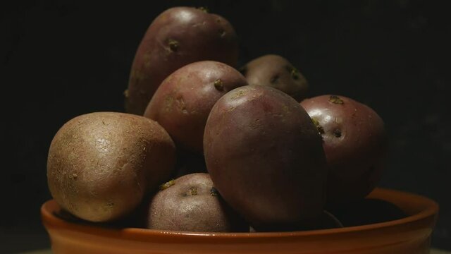A pile of potatoes in an earthen bowl spinning in the dark. Light paints different shadows on the subject. Playing with light and shadows on potatoes.