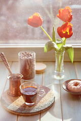 Oriental coffee in traditional copper coffee pot with flowers on window sill. Wooden windowsill with orange tulips and hyacinth flower pot. Cold rainy day in spring. Cozy scene, hygge concept.