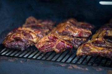 Smoke rising around a slow cooked beef brisket on the grill grates of a smoker barbecue. Grilled spare ribs macro - pork ribs