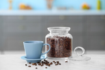 Cup and jar with coffee beans on table in modern kitchen