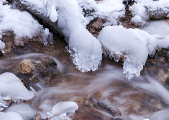 frozen fast flowing spring water, icy rocks and water stream, frosty tree roots, beautiful ice and water texture
