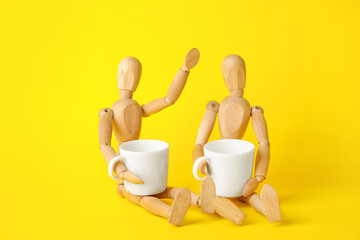Wooden mannequins with cups on color background