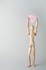 Wooden mannequin with pink heart on light background