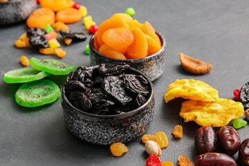 Bowls with different dried fruits on dark background