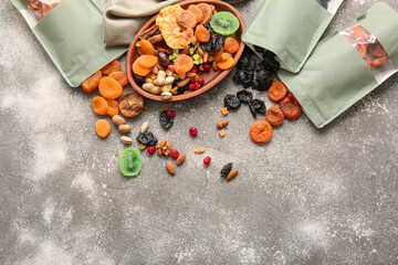 Fototapeta na wymiar Plate and bags with different dried fruits and nuts on gray background
