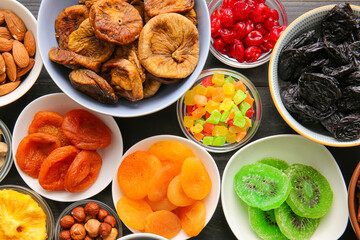 Bowls with different dried fruits and nuts on dark background