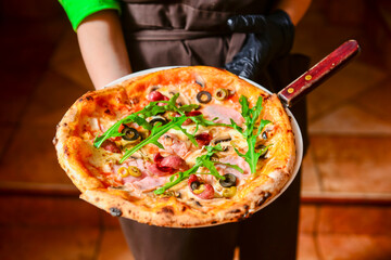 Bacon pizza with fresh greenery and olives served by waiter in restaurant or diner. Eating out concept, Italian cuisine.