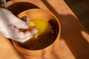 An adult woman's hand picks up bee honey from a brown clay bowl.