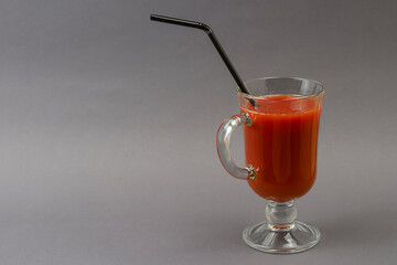 A full goblet of tomato juice with cocktail straw on a gray background.