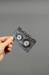 Handholds an audio cassette on a gray background.