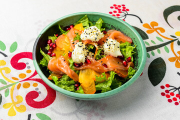 Delicious healthy salmon salad with cheese and pomegranate seeds served in a bowl over traditional Ukrainian tablecloth.