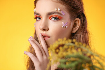 Portrait of beautiful young woman with creative makeup and flowers on color background