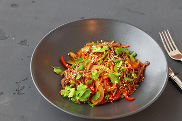 Bowl of wok noodles with vegetables on black background