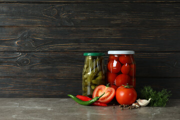 Jars with pickled tomatoes and cucumbers on wooden background