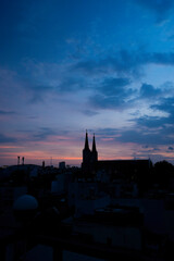 Fototapeta premium Beautiful red and blue sunrise sky with clouds over black silhouette of city with tower of church on horizon. Silhouette of the catholic church and cross