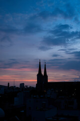 Obraz premium Beautiful red and blue sunrise sky with clouds over black silhouette of city with tower of church on horizon. Silhouette of the catholic church and cross
