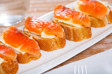 Naklejka na ściany i meble Slices of fresh baguette with butter and salmon. Tasty seafood appetizer..