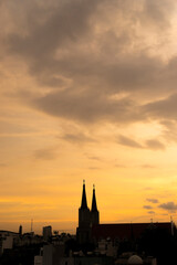 Fototapeta premium Beautiful red and blue sunrise sky with clouds over black silhouette of city with tower of church on horizon. Silhouette of the catholic church and cross
