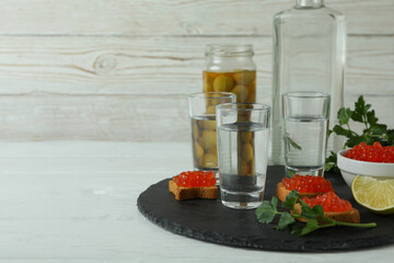 Shots of vodka and tasty snacks on white wooden background, space for text