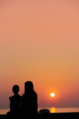Fototapeta na wymiar 海岸で綺麗な夕焼けを見ている子供姉妹の姿の風景