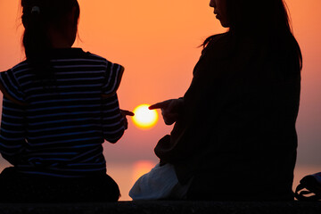 海岸で綺麗な夕焼けを見ている子供姉妹の姿の風景