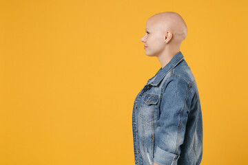 Side profile view of young bald caucasian positive nice attractive woman 20s without hair wearing casual denim jacket white t-shirt looking aside isolated on yellow color background studio portrait.