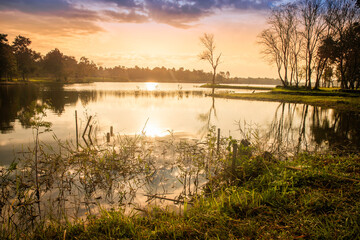 Fototapeta na wymiar Scenic view at beautiful spring sunset with reflection on a shiny lake with golden sun rays, calm water. cloudy sky and glow on a background, spring evening landscape