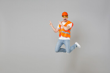 Full length young employee man in orange vest protective hardhat jump high point finger aside on...