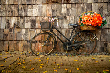 vintage bicycle decorated with flowers in basket parked in near old  wooden wall
