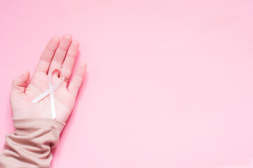 Women's hand with a pink ribbon is a symbol of the fight against breast cancer.