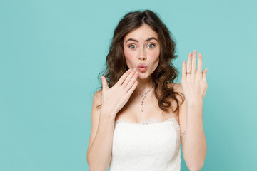Shocked bride young woman in beautiful white wedding dress showing finger with ring covering mouth...
