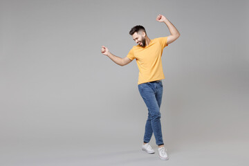 Full length of young bearded attractive smiling man 20s in casual yellow basic t-shirt with outstretched hand leaning over looking aside winner gesture isolated on grey background studio portrait.