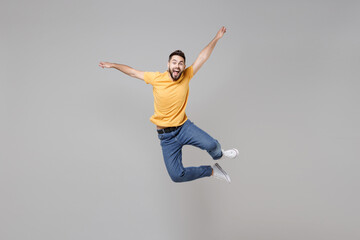 Fototapeta premium Full length of young bearded student smiling happy cheerful overjoyed man 20s in yellow basic t-shirt jump high looking camera flying outstretched hands isolated on grey background studio portrait..
